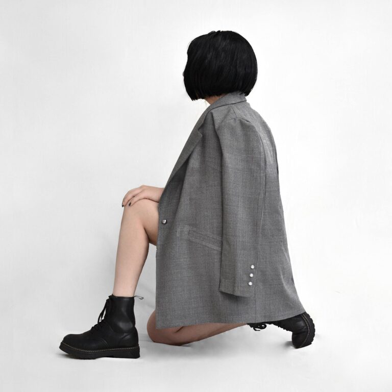 Side view of anonymous female in stylish jacket and leather boots squatting on white background